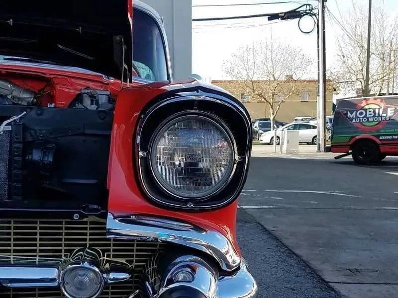 Close-up of a red classic car's headlight and chrome detailing with the hood open.