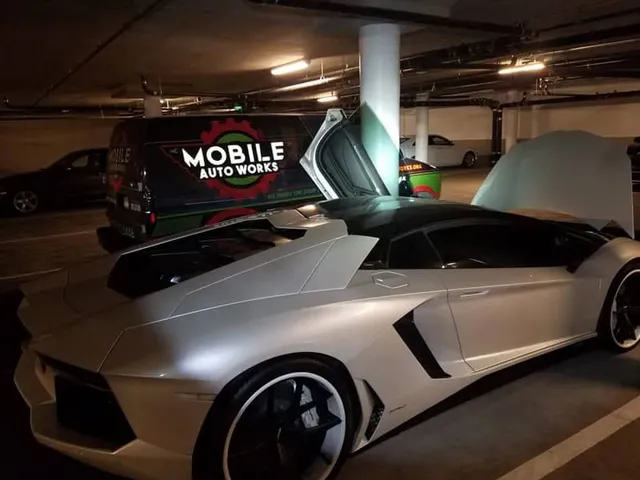 Silver Lamborghini with open doors being worked on near a Mobile Auto Works van in an underground garage.