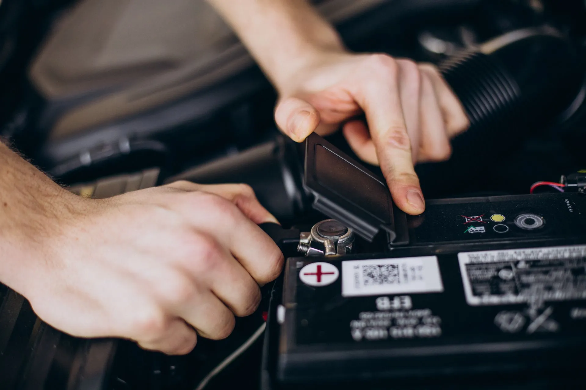 Hands connecting a battery terminal in a car engine compartment.